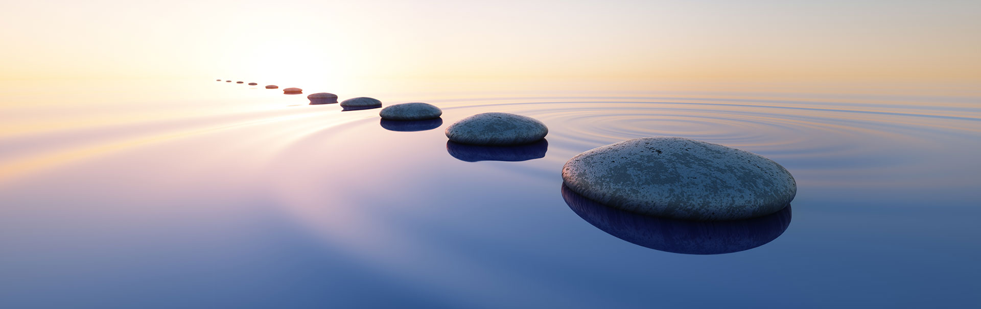 Stone path leading towards a serene sunset over a tranquil body of water.