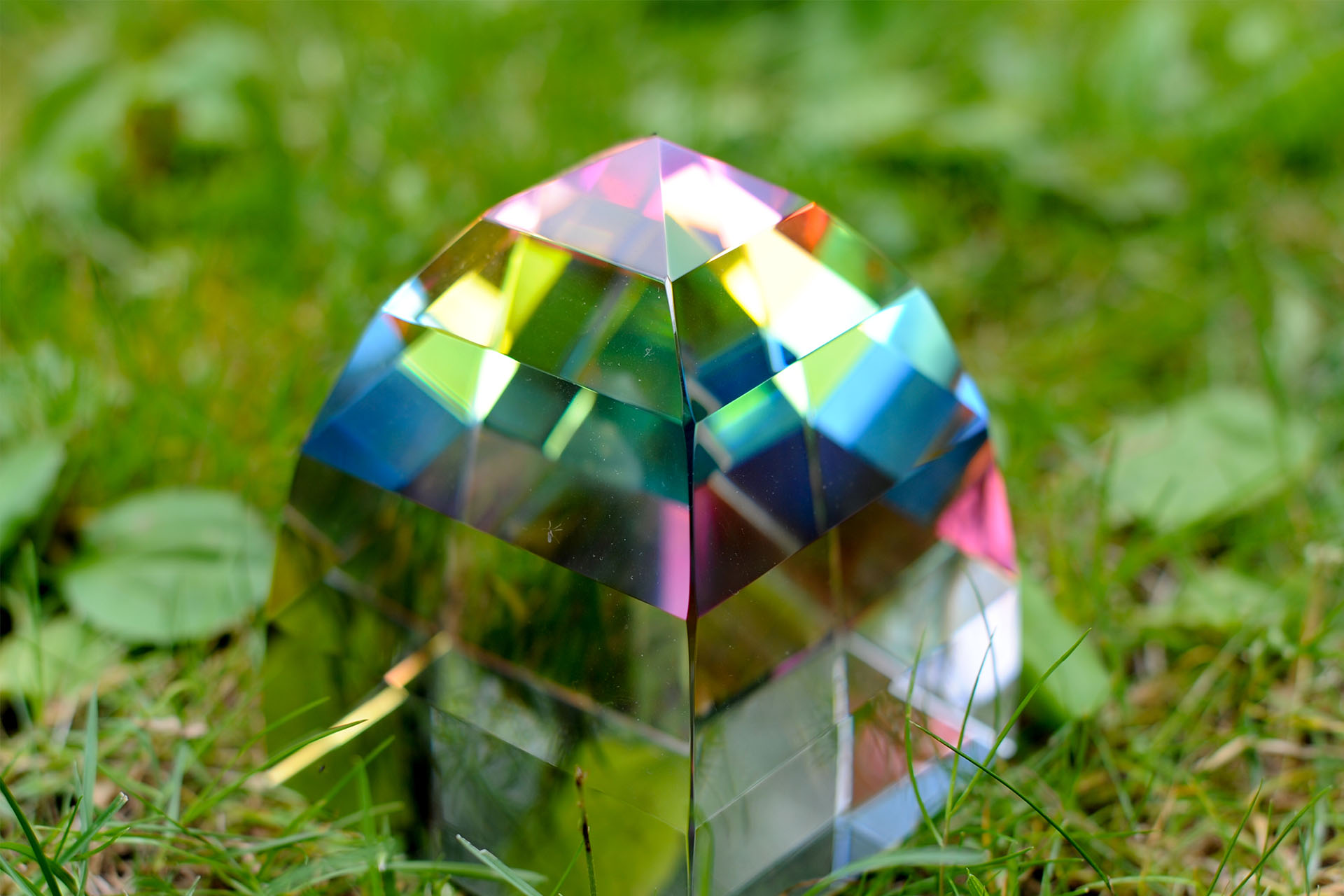 Alt text  A colorful crystal-like object with a faceted structure, resting on grass.